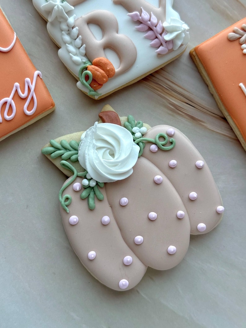 Assorted boho pumpkin baby shower sugar cookies decorated with pumpkins, baby onesie, baby bottle, rainbow, baby feet, “Little Pumpkin,” “Oh Baby,” “Baby Girl,” and “BABY” plaque in soft blush, sage, ivory, and pumpkin orange.