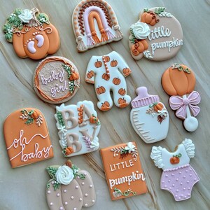 Assorted boho pumpkin baby shower sugar cookies decorated with pumpkins, baby onesie, baby bottle, rainbow, baby feet, “Little Pumpkin,” “Oh Baby,” “Baby Girl,” and “BABY” plaque in soft blush, sage, ivory, and pumpkin orange.