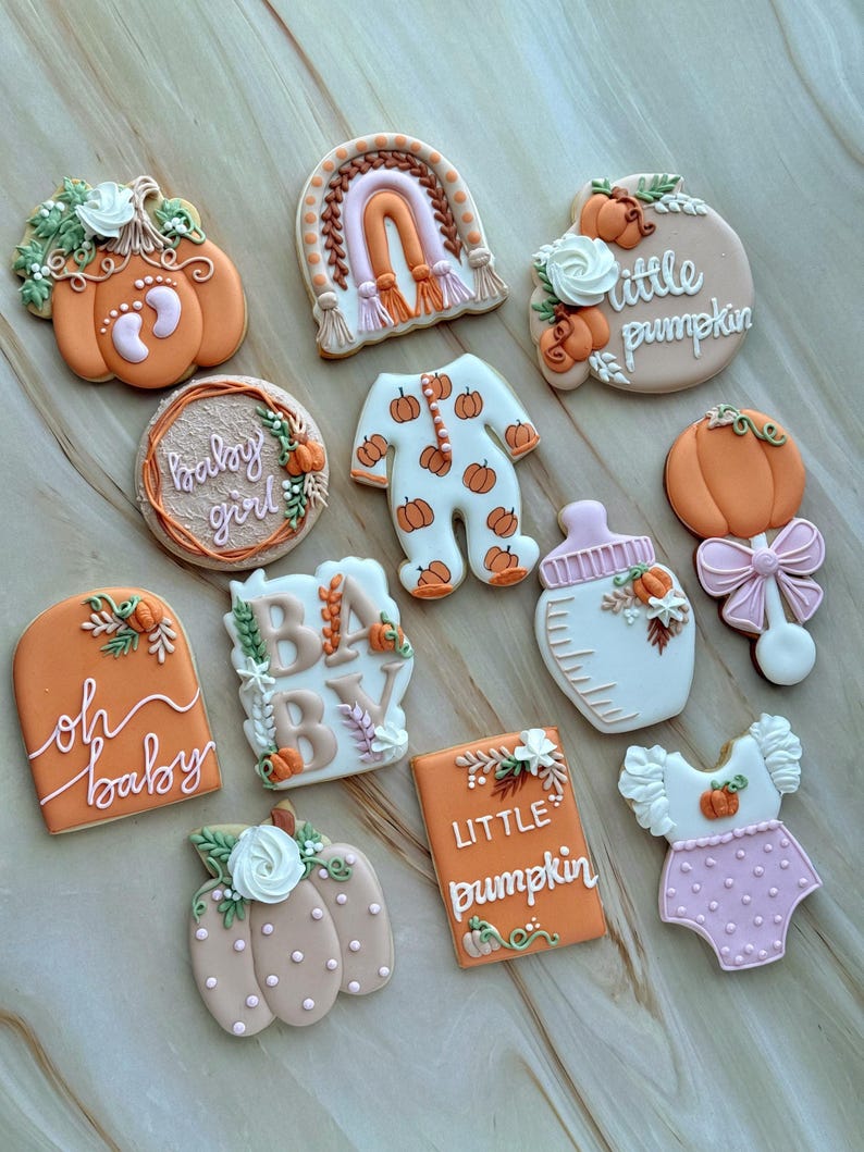 Assorted boho pumpkin baby shower sugar cookies decorated with pumpkins, baby onesie, baby bottle, rainbow, baby feet, “Little Pumpkin,” “Oh Baby,” “Baby Girl,” and “BABY” plaque in soft blush, sage, ivory, and pumpkin orange.