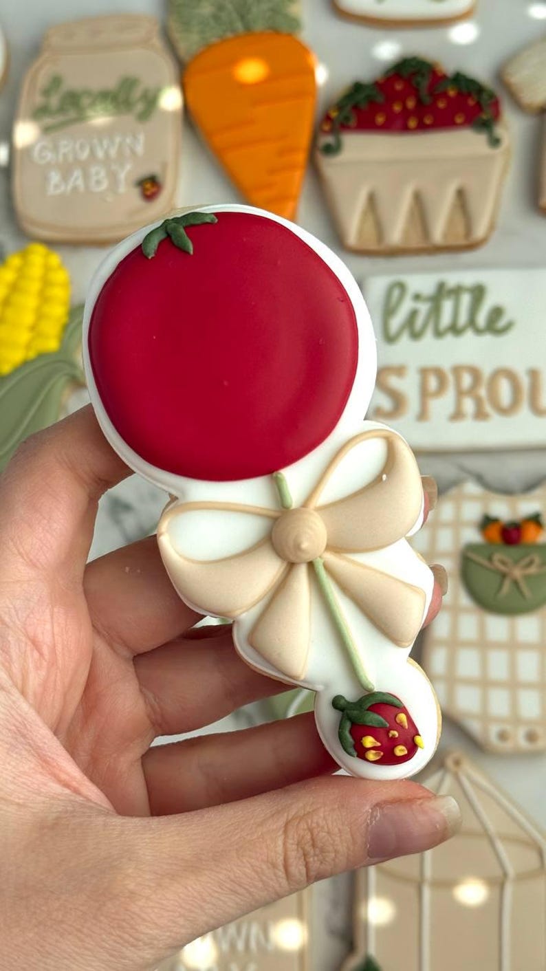Farmers market-themed baby shower sugar cookies featuring hand-decorated designs like “little sprout,” baby onesies with vegetables, carrots, corn, strawberries, tomatoes, baby bottles, mason jars, leafy greens, and baby mobiles. Adorned with soft green, beige, orange, and red royal icing, these custom cookies are perfect for a “locally grown” or garden baby shower theme, gender-neutral celebrations, and personalized baby gifts.