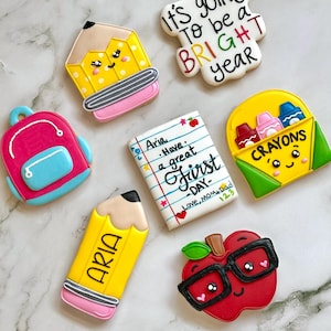 Peut inclure: Un ensemble de six biscuits décorés sur le thème de la rentrée scolaire. Les biscuits sont en forme de crayon, de sac à dos, de cahier, de boîte de crayons, de pomme et d'une pancarte qui dit "It's going to be a BRIGHT year".