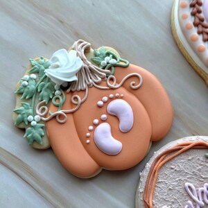 Assorted boho pumpkin baby shower sugar cookies decorated with pumpkins, baby onesie, baby bottle, rainbow, baby feet, “Little Pumpkin,” “Oh Baby,” “Baby Girl,” and “BABY” plaque in soft blush, sage, ivory, and pumpkin orange.