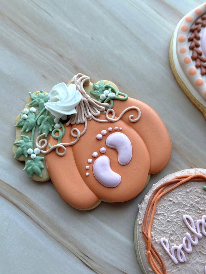 Assorted boho pumpkin baby shower sugar cookies decorated with pumpkins, baby onesie, baby bottle, rainbow, baby feet, “Little Pumpkin,” “Oh Baby,” “Baby Girl,” and “BABY” plaque in soft blush, sage, ivory, and pumpkin orange.