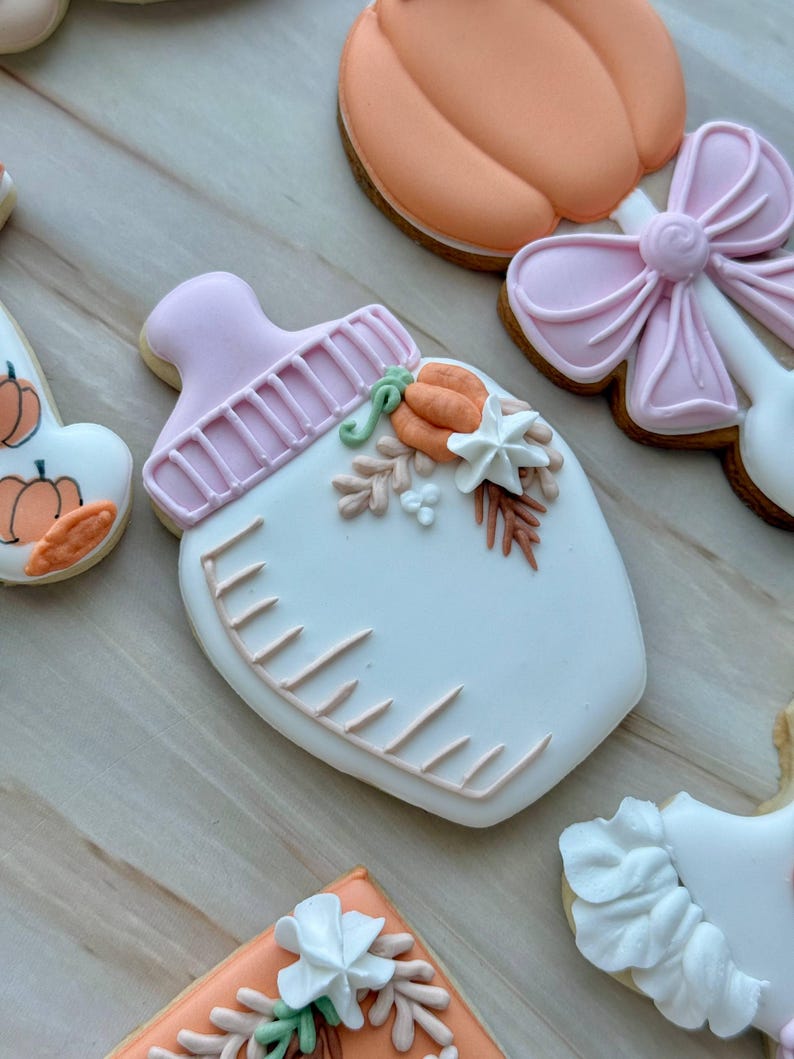 Assorted boho pumpkin baby shower sugar cookies decorated with pumpkins, baby onesie, baby bottle, rainbow, baby feet, “Little Pumpkin,” “Oh Baby,” “Baby Girl,” and “BABY” plaque in soft blush, sage, ivory, and pumpkin orange.