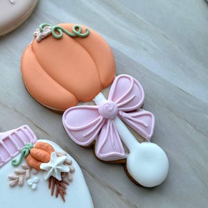 Assorted boho pumpkin baby shower sugar cookies decorated with pumpkins, baby onesie, baby bottle, rainbow, baby feet, “Little Pumpkin,” “Oh Baby,” “Baby Girl,” and “BABY” plaque in soft blush, sage, ivory, and pumpkin orange.