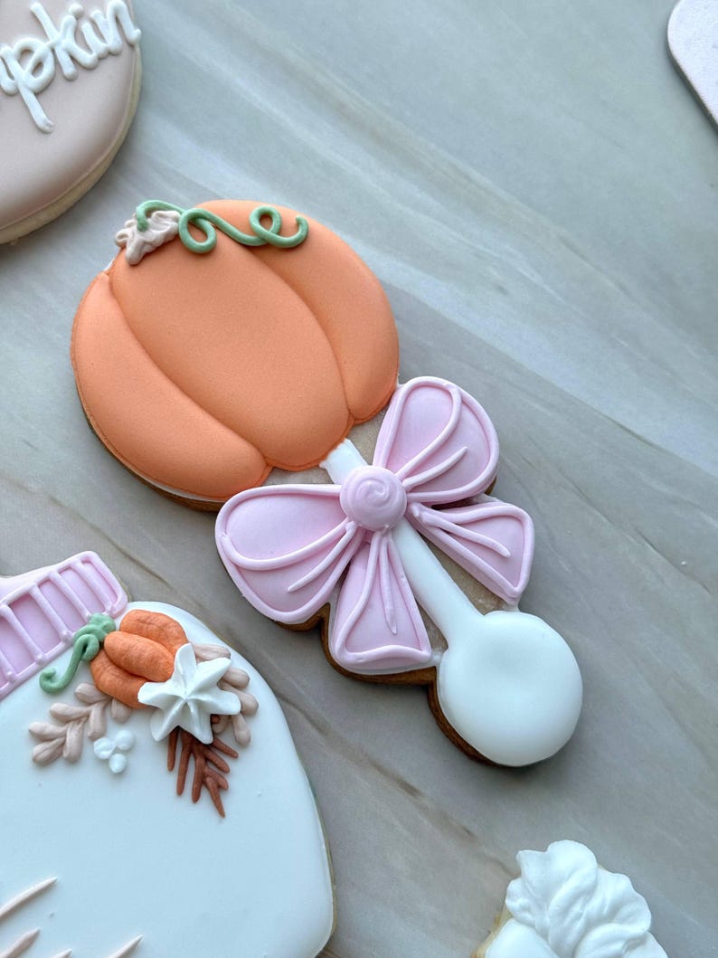 Assorted boho pumpkin baby shower sugar cookies decorated with pumpkins, baby onesie, baby bottle, rainbow, baby feet, “Little Pumpkin,” “Oh Baby,” “Baby Girl,” and “BABY” plaque in soft blush, sage, ivory, and pumpkin orange.