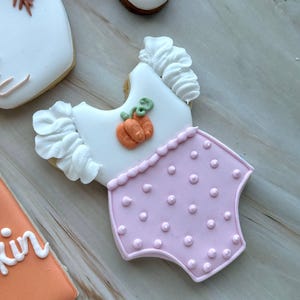 Assorted boho pumpkin baby shower sugar cookies decorated with pumpkins, baby onesie, baby bottle, rainbow, baby feet, “Little Pumpkin,” “Oh Baby,” “Baby Girl,” and “BABY” plaque in soft blush, sage, ivory, and pumpkin orange.