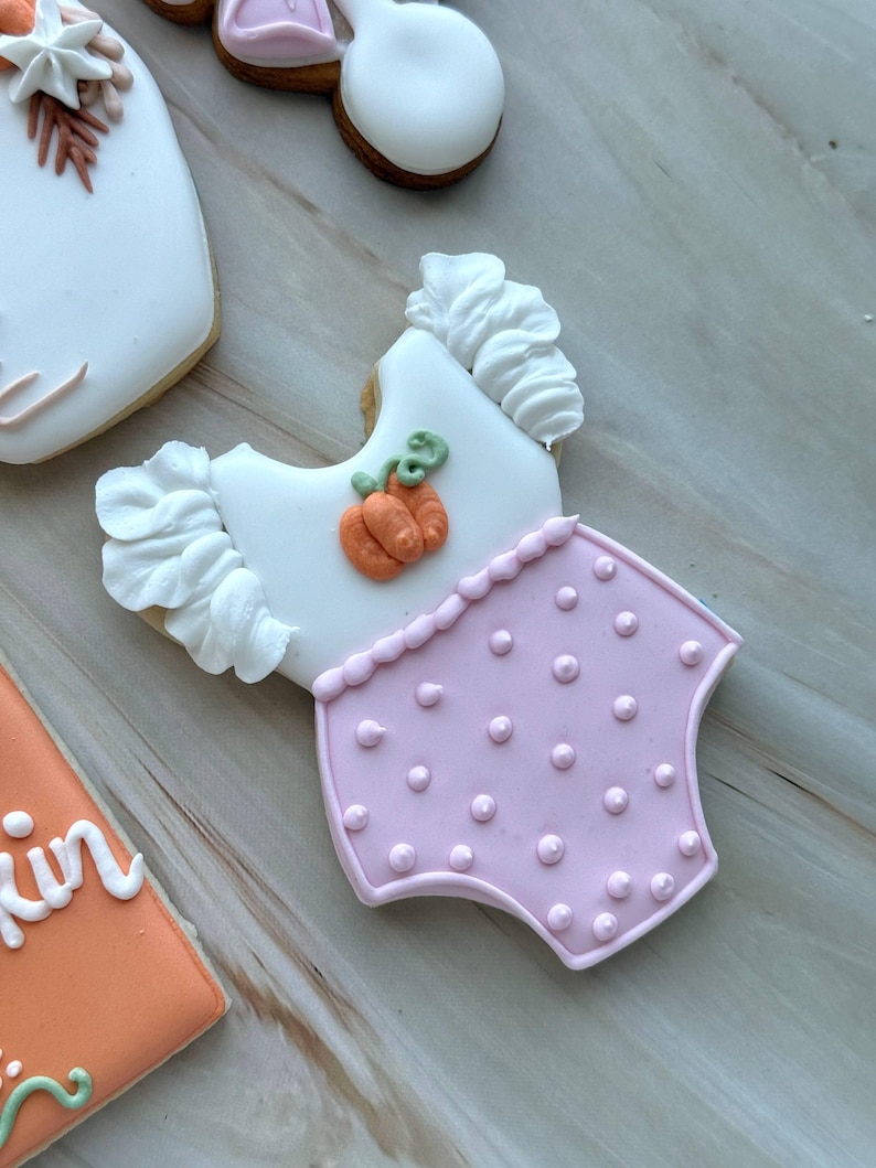 Assorted boho pumpkin baby shower sugar cookies decorated with pumpkins, baby onesie, baby bottle, rainbow, baby feet, “Little Pumpkin,” “Oh Baby,” “Baby Girl,” and “BABY” plaque in soft blush, sage, ivory, and pumpkin orange.