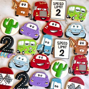 Può includere: Una collezione di biscotti di zucchero decorati con auto, cactus e il numero due. I biscotti sono decorati con vari colori, tra cui rosso, blu, verde, viola e marrone. I biscotti sono disposti su una superficie di marmo bianco. Il testo "SPEED LIMIT 2" e "Rust.eze" è visibile su alcuni dei biscotti.
