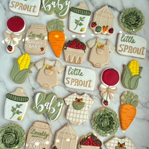 Farmers market-themed baby shower sugar cookies featuring hand-decorated designs like “little sprout,” baby onesies with vegetables, carrots, corn, strawberries, tomatoes, baby bottles, mason jars, leafy greens, and baby mobiles. Adorned with soft green, beige, orange, and red royal icing, these custom cookies are perfect for a “locally grown” or garden baby shower theme, gender-neutral celebrations, and personalized baby gifts.