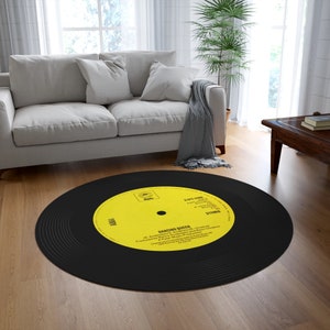 Op de afbeelding: Een rond vinyl platenkleed in zwart en geel met de tekst "Dancing Queen" en "A Polar Music Production" gedrukt op het label. Het kleed is rond en heeft een zwart midden met concentrische cirkels.