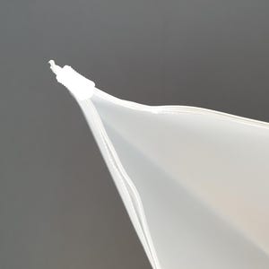 May include: Close-up of the top of a white zippered plastic bag. The zipper is closed and the bag is folded over at the top.