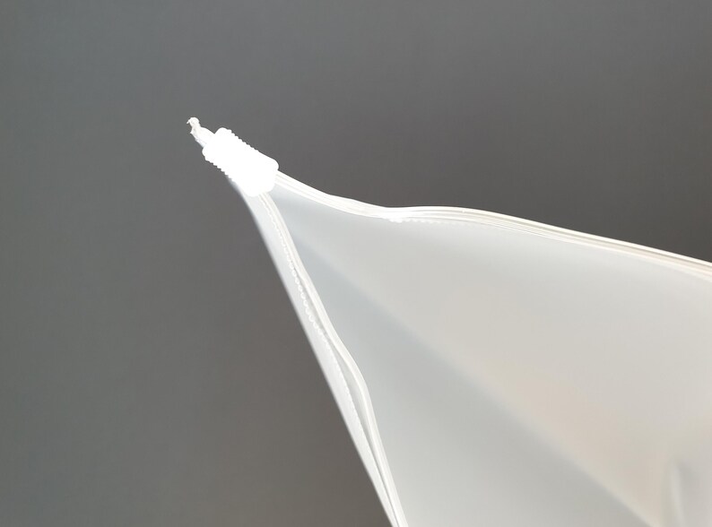 May include: Close-up of the top of a white zippered plastic bag. The zipper is closed and the bag is folded over at the top.