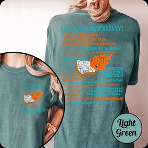 Puede incluir: Camiseta verde claro con el texto "It's Sandwich Day!" y una ilustraci&oacute;n de un pez de dibujos animados. La camiseta tambi&eacute;n presenta el texto "I can't give Pudge tuna" y "Pudge is a fish?"
