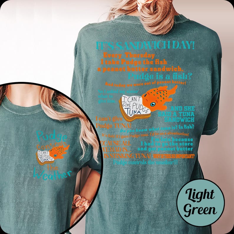 Puede incluir: Camiseta verde claro con el texto "It's Sandwich Day!" y una ilustraci&oacute;n de un pez de dibujos animados. La camiseta tambi&eacute;n presenta el texto "I can't give Pudge tuna" y "Pudge is a fish?"