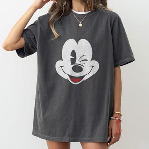 May include: A dark gray oversized t-shirt with a white Mickey Mouse graphic. Mickey Mouse is winking and smiling.