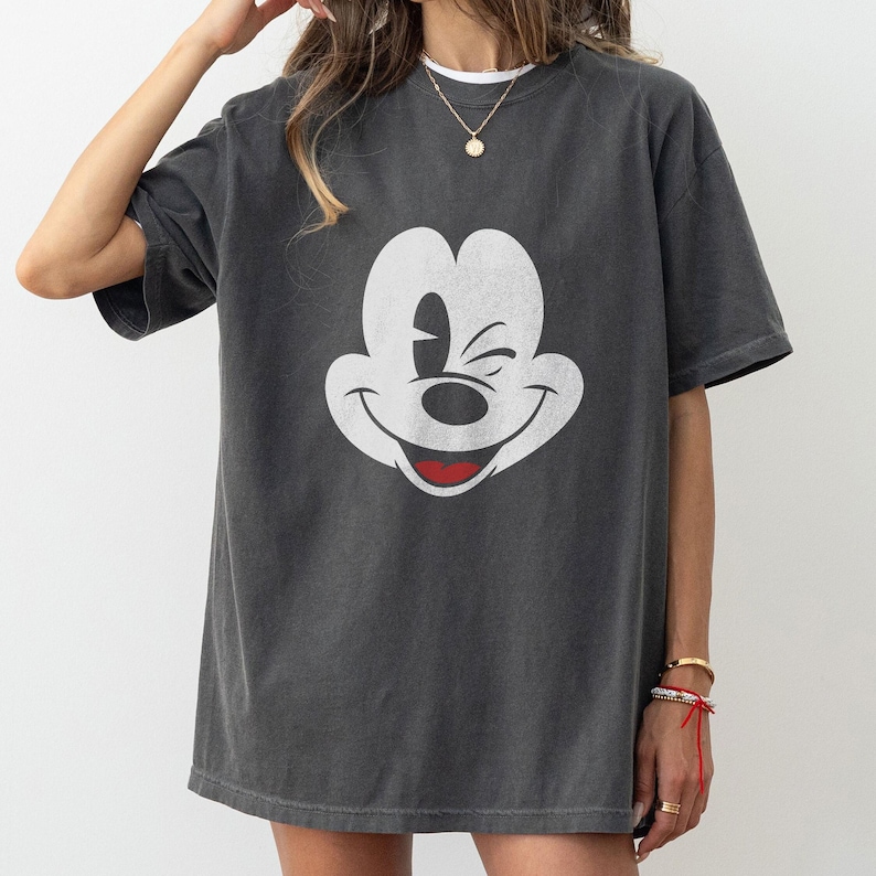 May include: A dark gray oversized t-shirt with a white Mickey Mouse graphic. Mickey Mouse is winking and smiling.