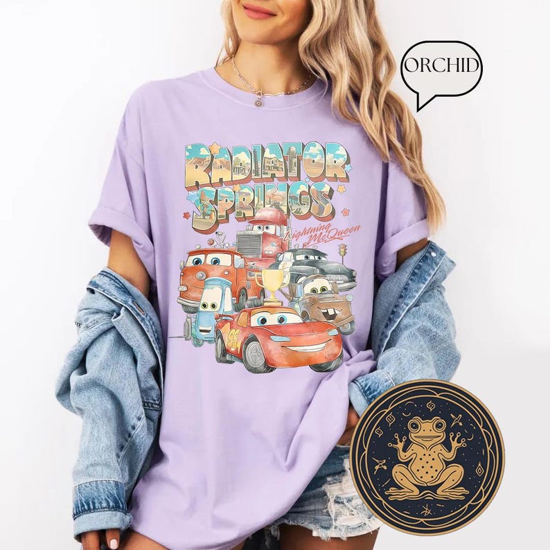 May include: A lavender t-shirt with a graphic print of the Cars characters from the movie Cars. The graphic includes the text "Radiator Springs" and "Lightning McQueen".