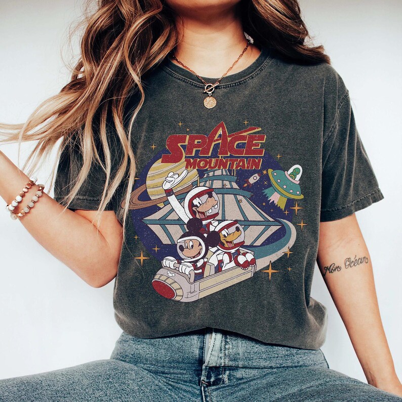 K&ouml;nnte beinhalten: Ein dunkelgraues T-Shirt mit einem Vintage-Grafikdruck von Mickey Mouse und Donald Duck, die in einem Raumschiff sitzen. Der Druck enth&auml;lt den Text "Space Mountain".