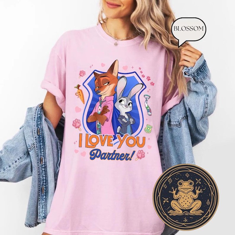 May include: Pink t-shirt featuring a cartoon illustration of Nick Wilde and Judy Hopps from Zootopia, with the text "I Love You Partner!". The design includes a carrot, paw prints, and a tie. The shirt is a light pink color.