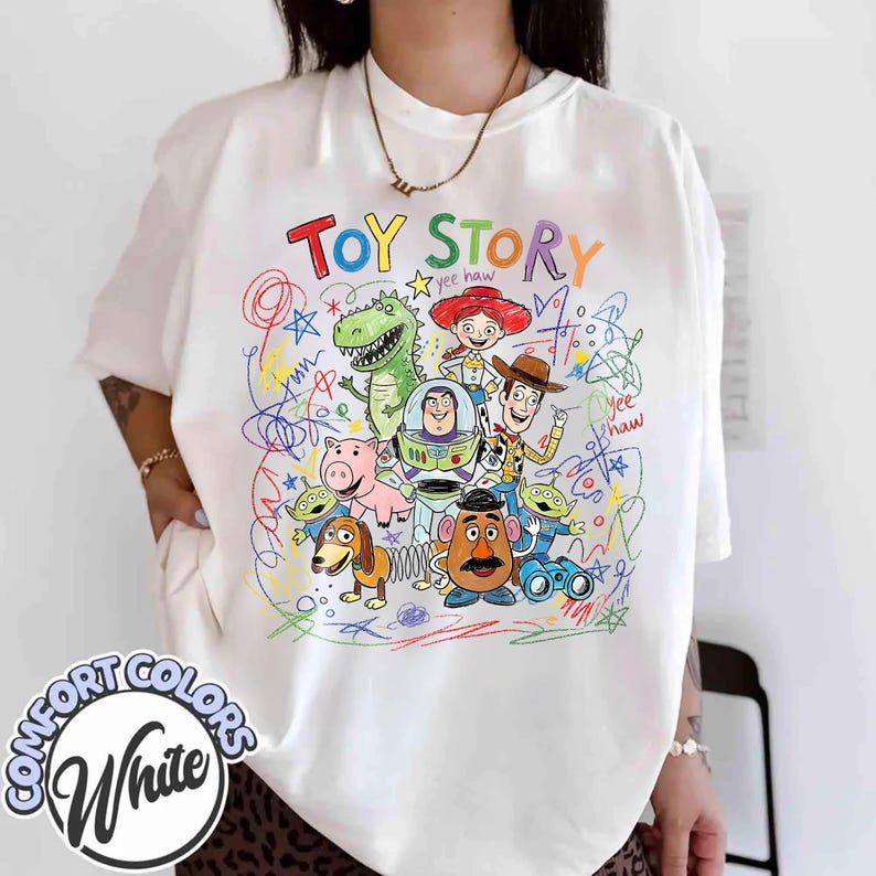 K&ouml;nnte beinhalten: Wei&szlig;es Comfort Colors T-Shirt mit einem farbenfrohen Toy Story-Charakter-Design. Das Design zeigt Woody, Buzz Lightyear, Jessie, Rex und andere Charaktere mit dem Schriftzug "Toy Story". Das T-Shirt hat eine lockere Passform.