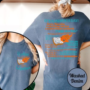 Puede incluir: Camiseta de mezclilla azul lavado con un dise&ntilde;o gr&aacute;fico. El dise&ntilde;o incluye el texto "IT'S SANDWICH DAY!" y "I CAN'T GIVE PUDGE TUNA". Tambi&eacute;n hay una ilustraci&oacute;n de un pez naranja. La camiseta tiene cuello redondo.