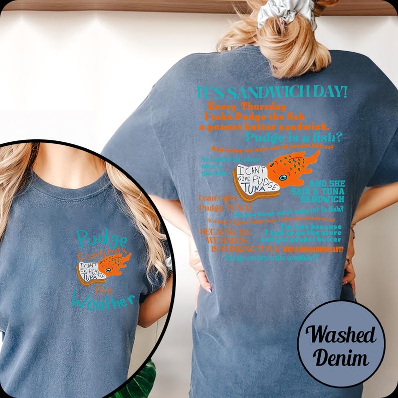Puede incluir: Camiseta de mezclilla azul lavado con un dise&ntilde;o gr&aacute;fico. El dise&ntilde;o incluye el texto "IT'S SANDWICH DAY!" y "I CAN'T GIVE PUDGE TUNA". Tambi&eacute;n hay una ilustraci&oacute;n de un pez naranja. La camiseta tiene cuello redondo.