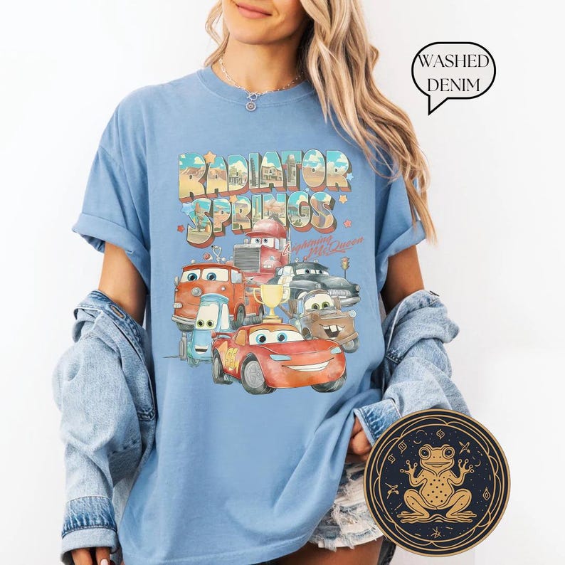 May include: A light blue t-shirt with a graphic of the Cars characters from the movie Cars. The graphic includes the text "Radiator Springs" and "Welcome to McQueen".