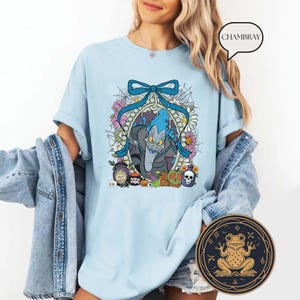 Op de afbeelding: Lichtblauw T-shirt met een cartoon illustratie van Hades uit Disney's Hercules. Het ontwerp bevat een blauwe strik, bloemen en Halloween-thema-elementen. Het shirt heeft een relaxte pasvorm.