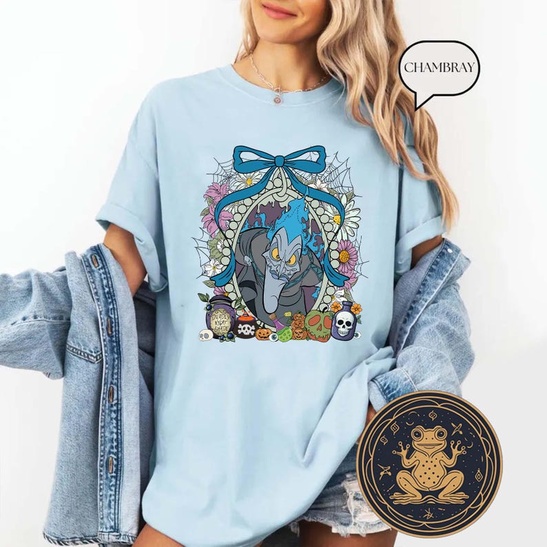 Op de afbeelding: Lichtblauw T-shirt met een cartoon illustratie van Hades uit Disney's Hercules. Het ontwerp bevat een blauwe strik, bloemen en Halloween-thema-elementen. Het shirt heeft een relaxte pasvorm.