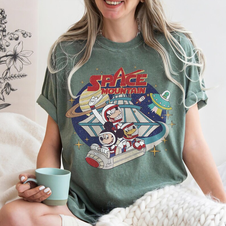 K&ouml;nnte beinhalten: Ein gr&uuml;nes T-Shirt mit einem Vintage-Grafikdruck von Mickey Mouse, Donald Duck und Goofy, die eine Space Mountain-Fahrt machen. Der Text "SPACE MOUNTAIN" ist &uuml;ber den Figuren gedruckt.