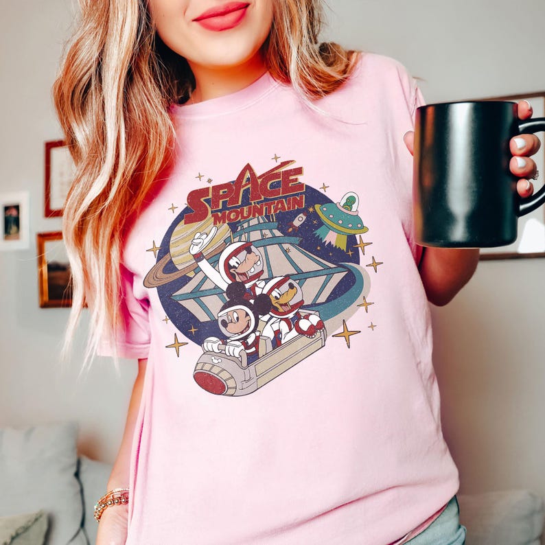 K&ouml;nnte beinhalten: Rosafarbenes T-Shirt mit einem Vintage-Grafikdruck von Mickey Mouse, Donald Duck und Goofy, die auf der Space Mountain fahren. Die Grafik enth&auml;lt den Text "Space Mountain".