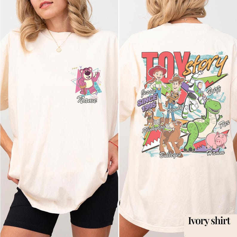 May include: Ivory-colored t-shirt featuring a front pocket design with a cartoon bear and the word "Name". The back of the shirt displays the text "Toy Story" and various cartoon characters, including Woody and Buzz Lightyear.