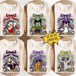 Op de afbeelding: Zes cr&egrave;mekleurige T-shirts met Halloween-thema Disney-personages. Elk shirt toont een ander personage, zoals Donald Duck, Mickey Mouse en Minnie Mouse, in een decoratief ovaal frame met een strik en bloemmotieven. De tekst "WE DO ALL CHARACTER" staat in een gele ster.
