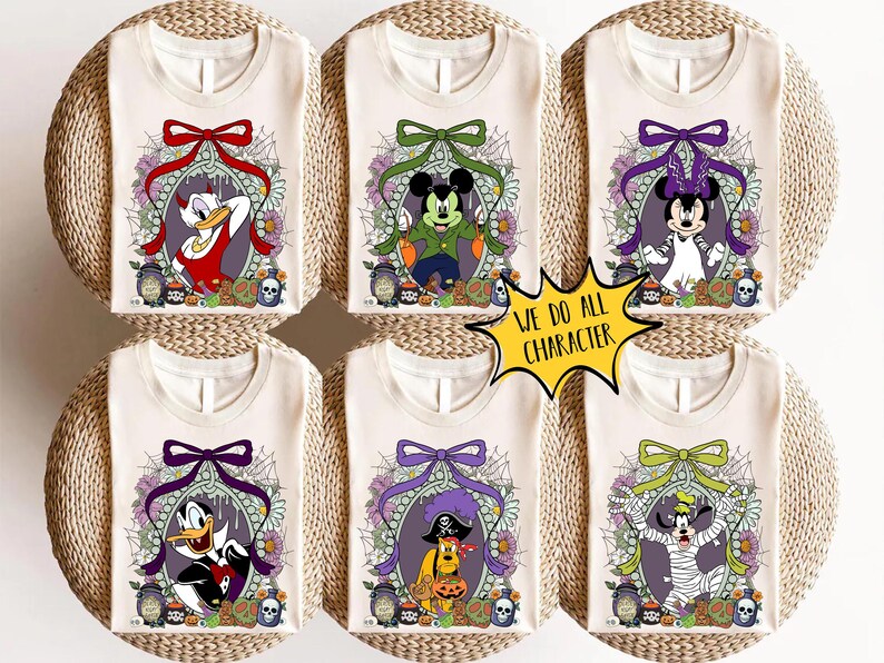 Op de afbeelding: Zes cr&egrave;mekleurige T-shirts met Halloween-thema Disney-personages. Elk shirt toont een ander personage, zoals Donald Duck, Mickey Mouse en Minnie Mouse, in een decoratief ovaal frame met een strik en bloemmotieven. De tekst "WE DO ALL CHARACTER" staat in een gele ster.