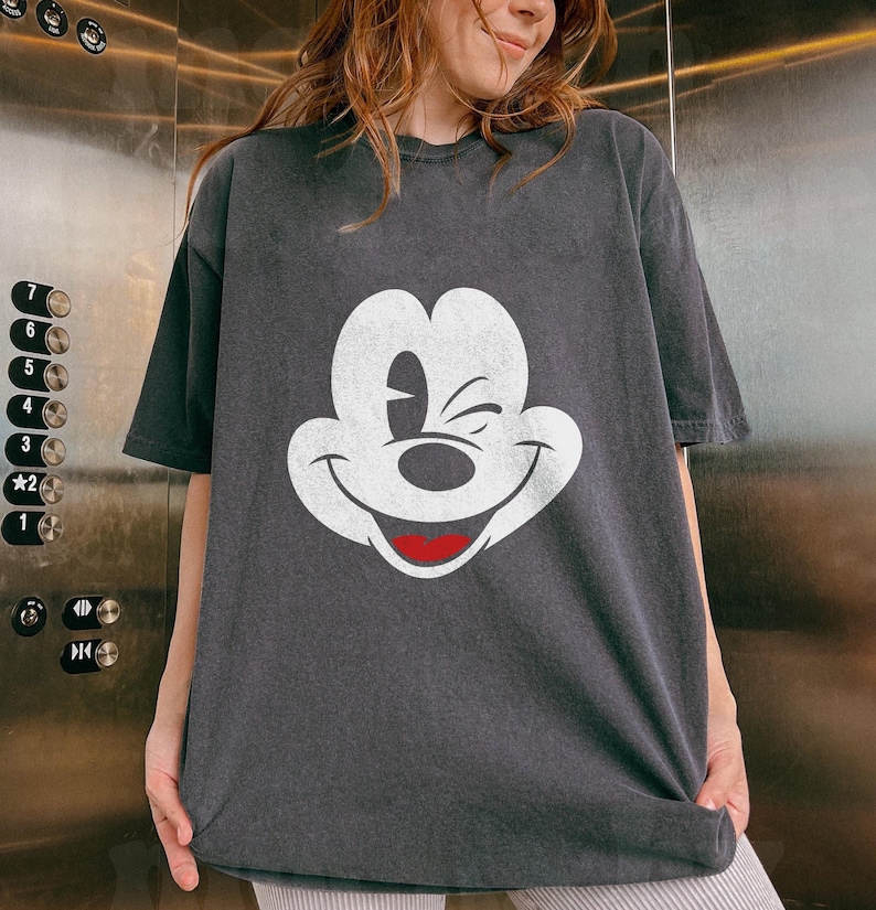 May include: A black t-shirt with a white graphic of Mickey Mouse winking. The graphic is distressed and has a vintage look.