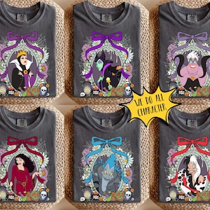 Op de afbeelding: Zes grijze t-shirts met Disney-schurk ontwerpen. Elk shirt toont een ander personage in een bloemenframe, bekroond met een strik. De tekst "WE DO ALL CHARACTER" staat in een gele ster. De shirts zijn gerangschikt op een geweven oppervlak.