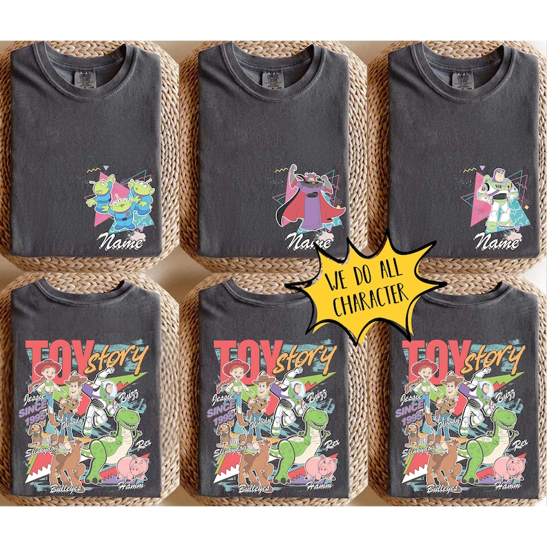 May include: Six charcoal gray t-shirts featuring Toy Story characters. Designs include the aliens, Zurg, and Buzz Lightyear, with personalized names. The bottom shirts display a larger Toy Story graphic with multiple characters.