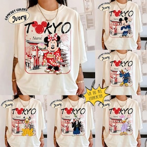 May include: Ivory-colored t-shirts with a graphic featuring a Disney character in traditional Japanese attire, the word "TOKYO", and a customizable name field. The shirts have a Comfort Colors label.