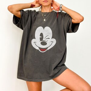 May include: A dark gray oversized t-shirt with a white Mickey Mouse graphic. Mickey Mouse is winking and smiling.
