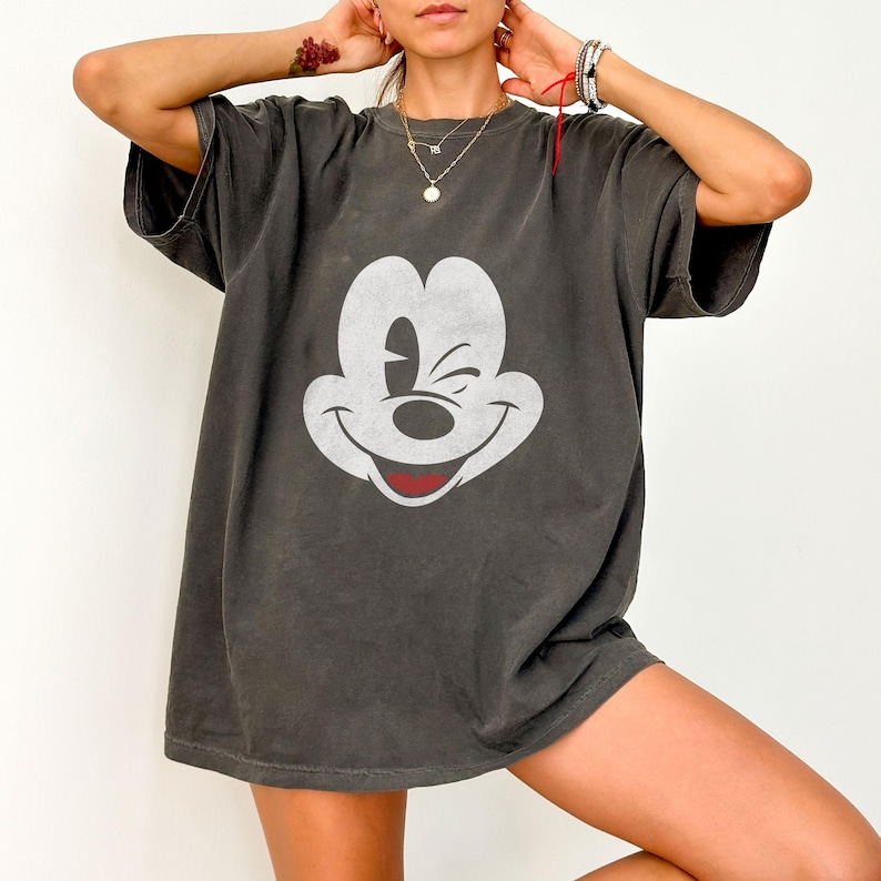 May include: A dark gray oversized t-shirt with a white Mickey Mouse graphic. Mickey Mouse is winking and smiling.