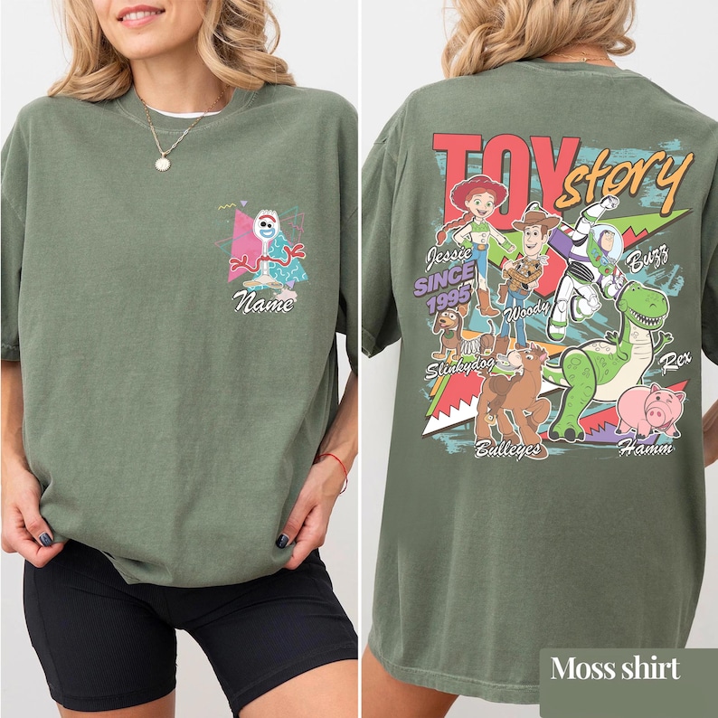 May include: Moss green t-shirt featuring a Toy Story design. The front has a cartoon character and the word "Name". The back displays the Toy Story logo and characters including Woody, Buzz, and Rex. The shirt is a relaxed fit.