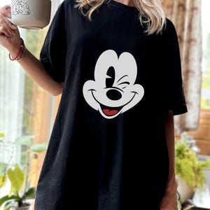 May include: Black oversized t-shirt with a white cartoon Mickey Mouse face graphic. The cartoon character is winking and smiling.