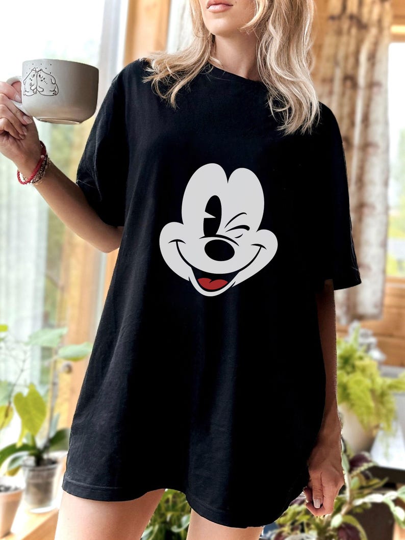 May include: Black oversized t-shirt with a white cartoon Mickey Mouse face graphic. The cartoon character is winking and smiling.