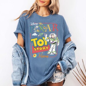 Peut inclure: T-shirt bleu avec le logo Disney Pixar Toy Story et Buzz l'&Eacute;clair. Le design comprend les mots "Disney Pixar Toy Story" en lettres color&eacute;es et une image de dessin anim&eacute; de Buzz l'&Eacute;clair.