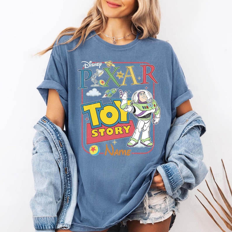 Peut inclure: T-shirt bleu avec le logo Disney Pixar Toy Story et Buzz l'&Eacute;clair. Le design comprend les mots "Disney Pixar Toy Story" en lettres color&eacute;es et une image de dessin anim&eacute; de Buzz l'&Eacute;clair.