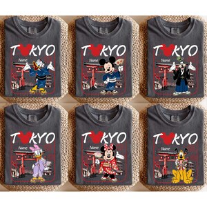 May include: Six gray t-shirts with the word "TOKYO" in white and a red heart. Each shirt features a different Disney character in traditional Japanese attire, with the text "Name" below the word "TOKYO".