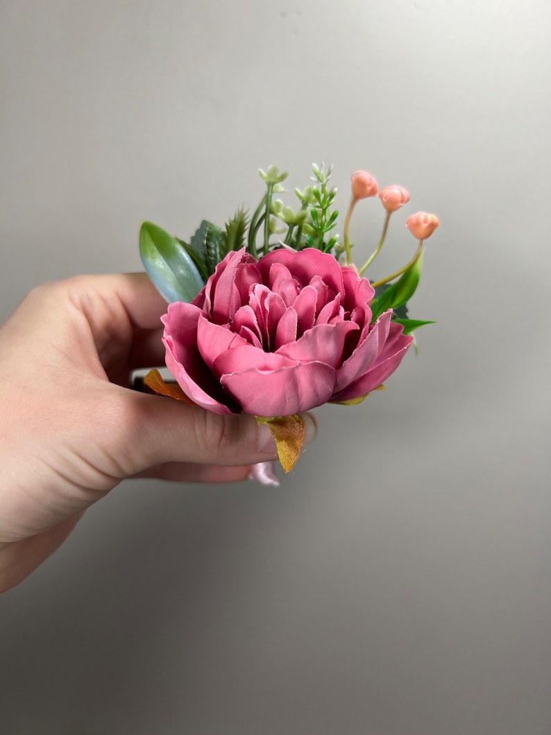 May include: A pink peony flower with green leaves and small pink buds. The flower is arranged in a bouquet.