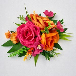 May include: A vibrant floral arrangement featuring a large, hot pink rose and several orange roses. Accented with smaller pink flowers, green leaves, and sprigs of yellow and orange. The flowers are clustered together, creating a full, lush appearance.
