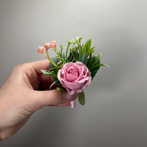 May include: A pink rose boutonniere with greenery and small pink buds.